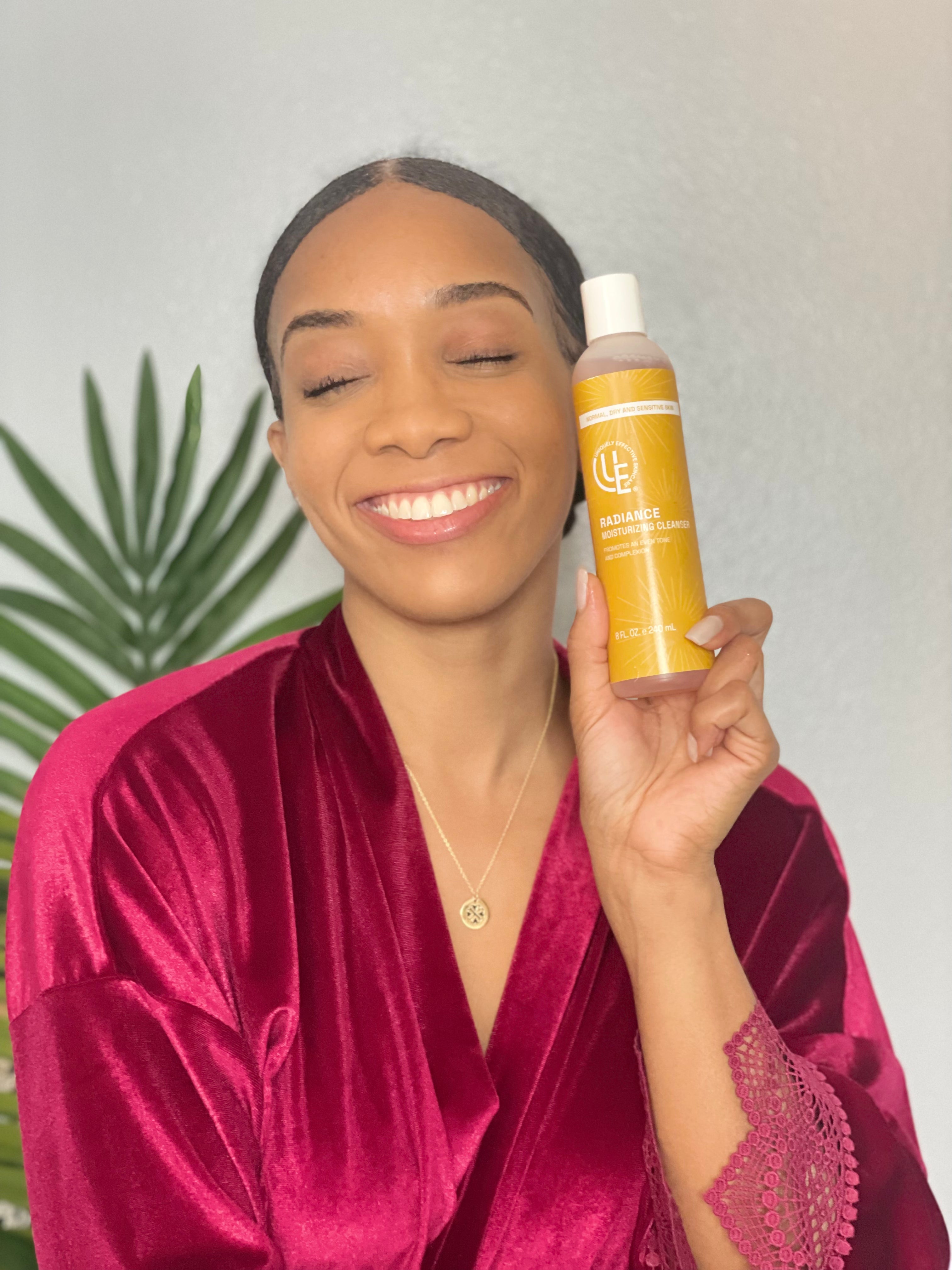 Beautiful woman with smooth and glowing complexion  holding bottle of Radiance Moisturizing Face Cleanser – hydrating daily gel cleanser for normal, dry, and sensitive skin that softens, nourishes, and promotes a natural glow.